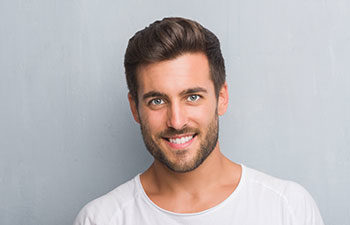 Handsome young man over grey grunge wall with a happy face